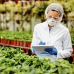 Female scientist writing notes while examining plants in a greenhouse.