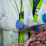 Technician using digital tablet while examining meat at meat factory