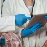 Technician using digital tablet while examining meat at meat factory